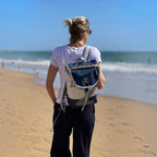 Lieblingstasche Landgang Mini backpack made from recycled blue and white sailcloth worn by a woman on the beach