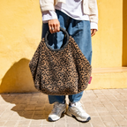 Lieblingstasche Loopbag Hobo in leopard print faux fur with a black circular handle held against a yellow wall