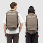 Lieblingstasche Lisbon Duffle Backpack M in taupe worn by a man and a woman against a light grey background