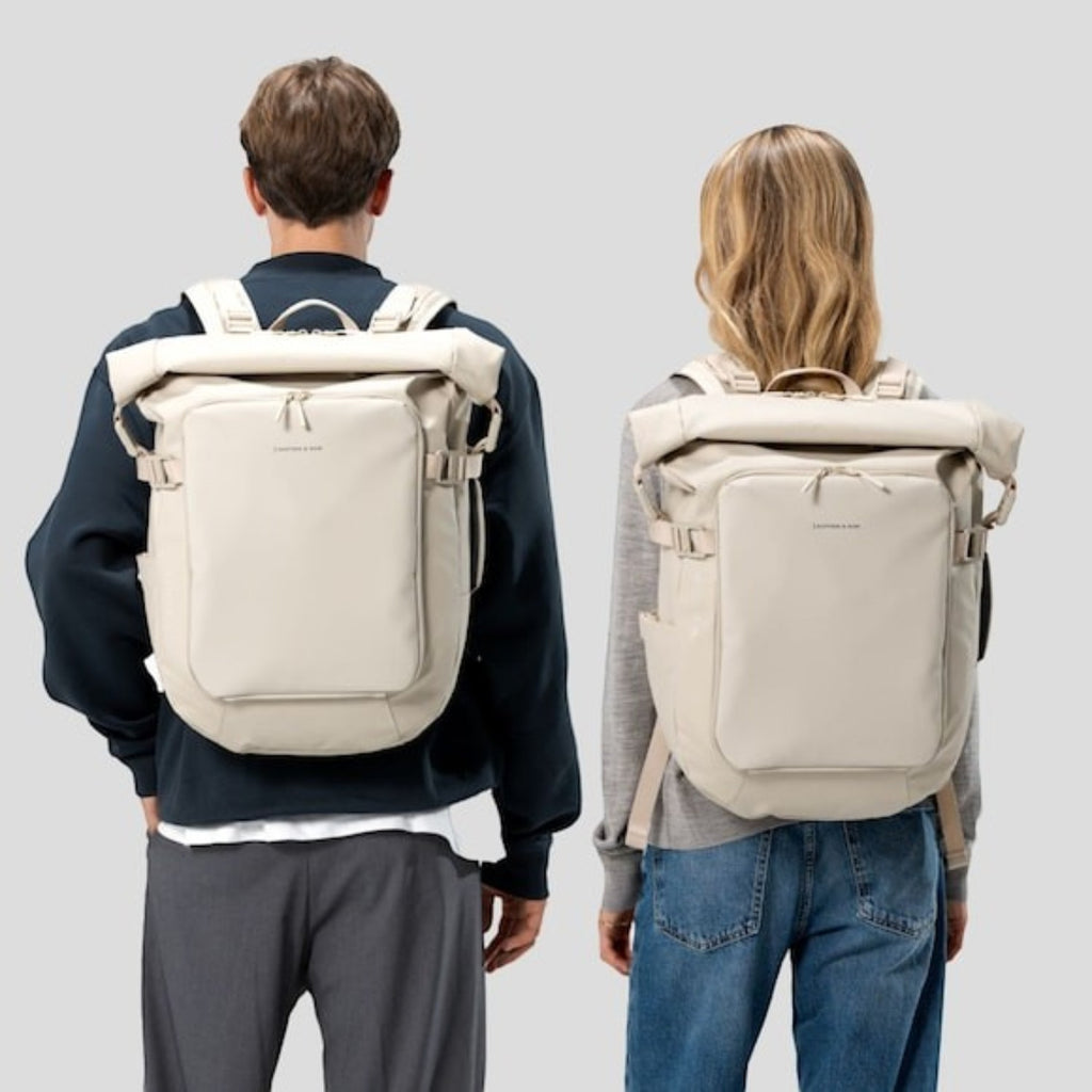 Lieblingstasche Lisbon Pro beige rolltop travel backpack worn by a man and a woman against a light grey background.