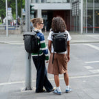 Two women wearing black Lieblingstasche Lisbon Small backpacks while standing on a city street.