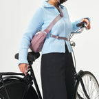 A woman wearing a mauve Lieblingstasche sling bag across her chest while standing next to a bicycle.