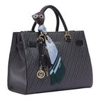 Lieblingstasche Tote M in black with monogram print, braided handles, and a decorative patterned silk scarf charm.