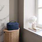 Lieblingstasche navy blue beautycase sitting on a woven wicker basket in a bright, minimalist bathroom setting