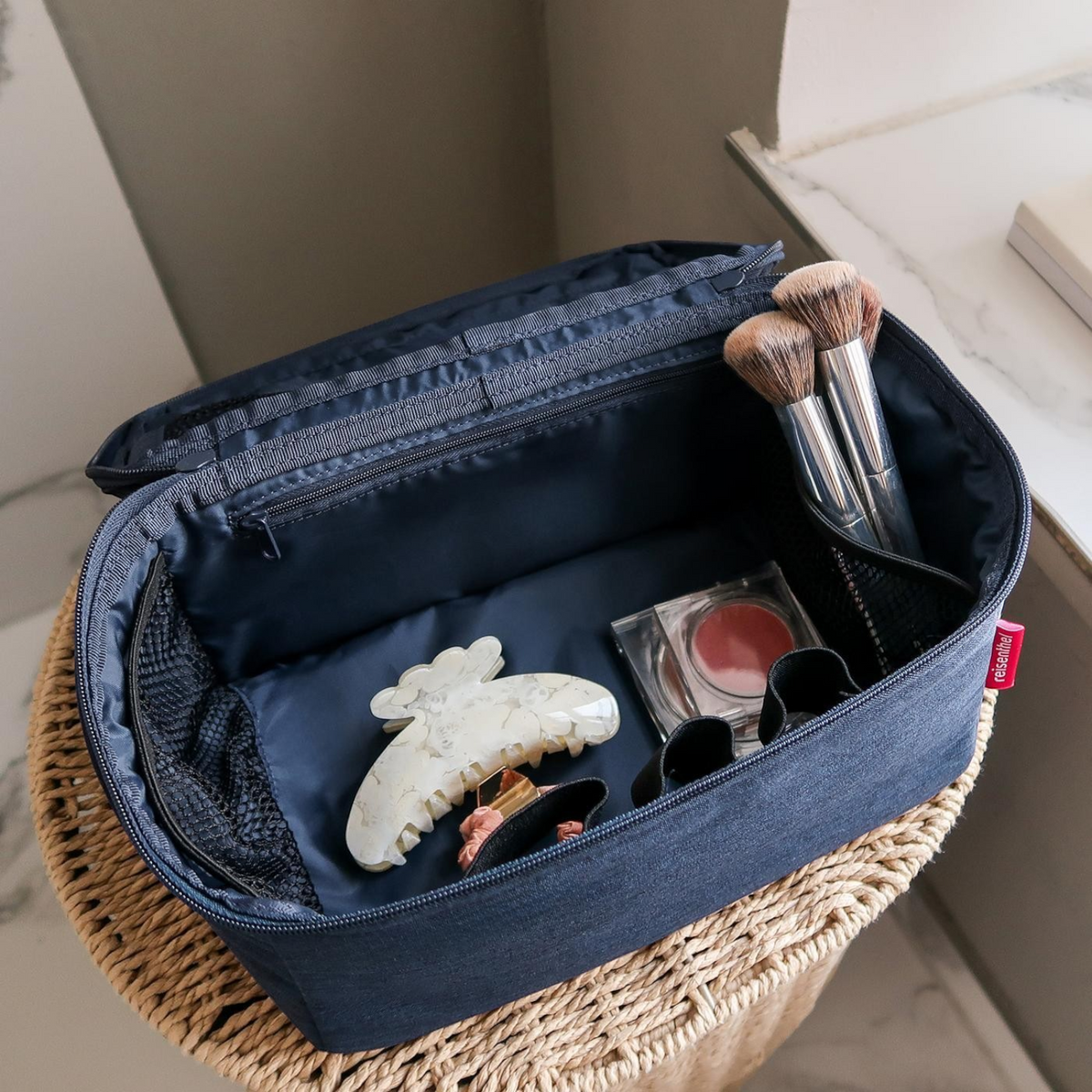 Lieblingstasche navy blue beautycase with organized makeup brushes and accessories inside on a wicker stool