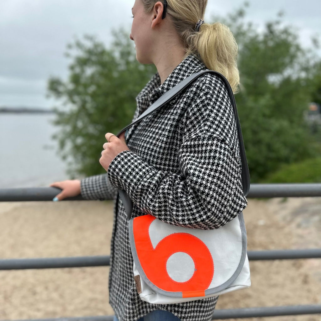 Lieblingstasche Perle white messenger bag with a bold orange circular logo worn over the shoulder by a woman