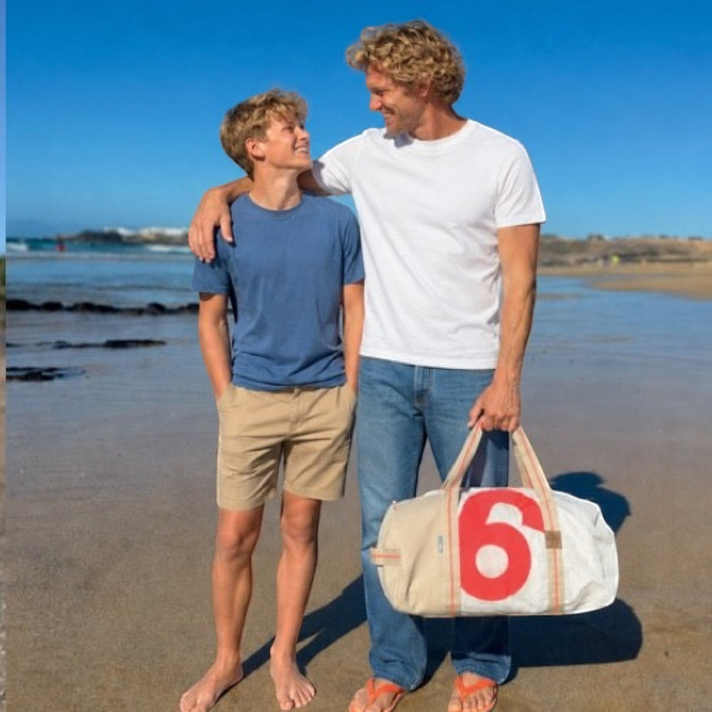 Lieblingstasche Pirat duffel bag with red number 6 print held by a man on a sunny beach with a teenager