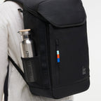 Lieblingstasche Pro Pack black backpack with side mesh pocket holding a metal water bottle, worn on a person's back.