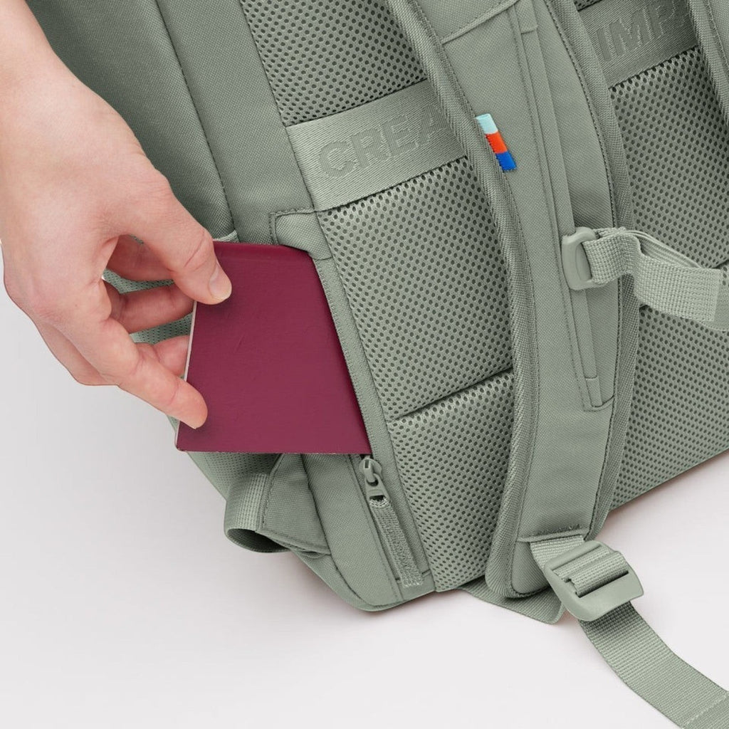 Lieblingstasche Pro Pack sage green backpack with a hand placing a passport into the hidden back security pocket