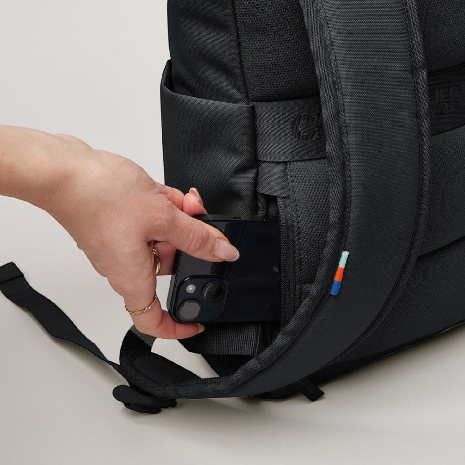 Lieblingstasche Rolltop Easy Small black backpack showing a hand placing a smartphone into the hidden back pocket.