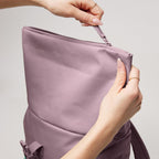 Lieblingstasche Rolltop Easy Small lilac canvas backpack being zipped closed by hands.
