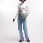 Model wearing a sage green GOT BAG Moon Bag Large crossbody, styled with a white turtleneck and blue jeans.