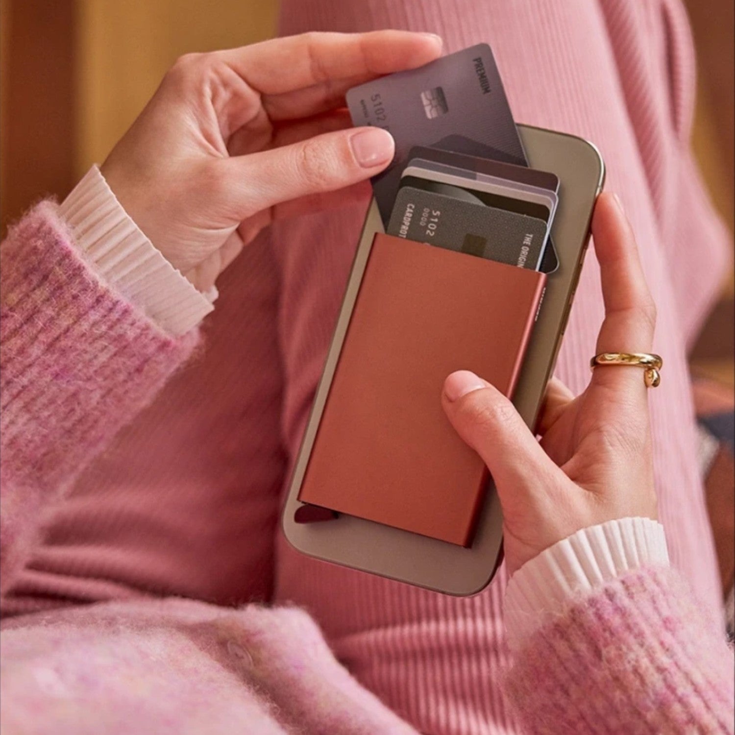 Lieblingstasche Secrid MagSafe card protector in terracotta attached to a smartphone with cards being accessed