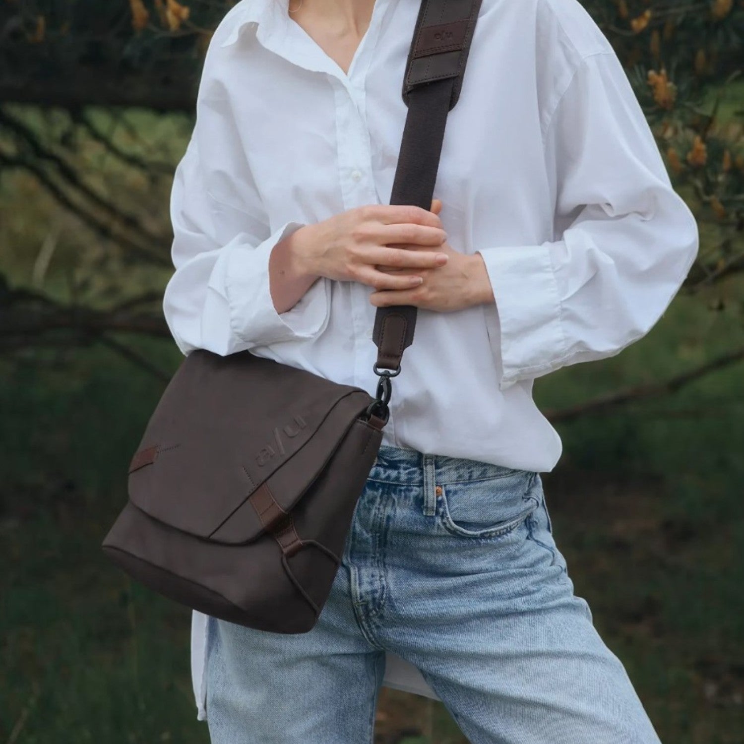 Lieblingstasche Sendai dark brown messenger bag worn crossbody by a woman in a white shirt and blue jeans