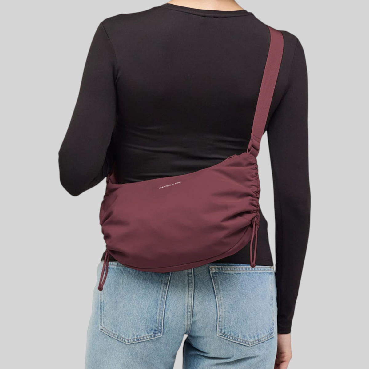 Lieblingstasche Skara Small burgundy crossbody bag with ruched sides worn by a woman in a black long-sleeve top
