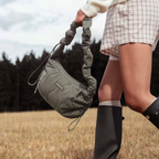 Lieblingstasche Skara Small Quilted olive green shoulder bag with ruched strap held by a woman in a field