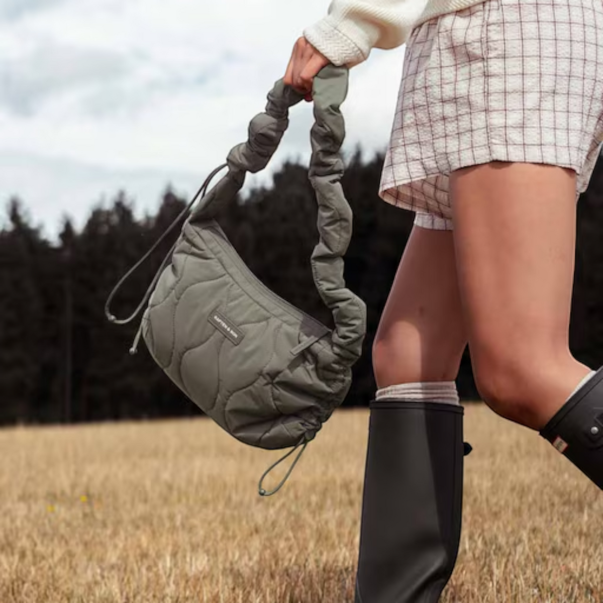 Lieblingstasche Skara Small Quilted olive green shoulder bag with ruched strap held by a woman in a field