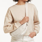 Lieblingstasche small moon bag in light beige, worn crossbody by a woman with curly hair.