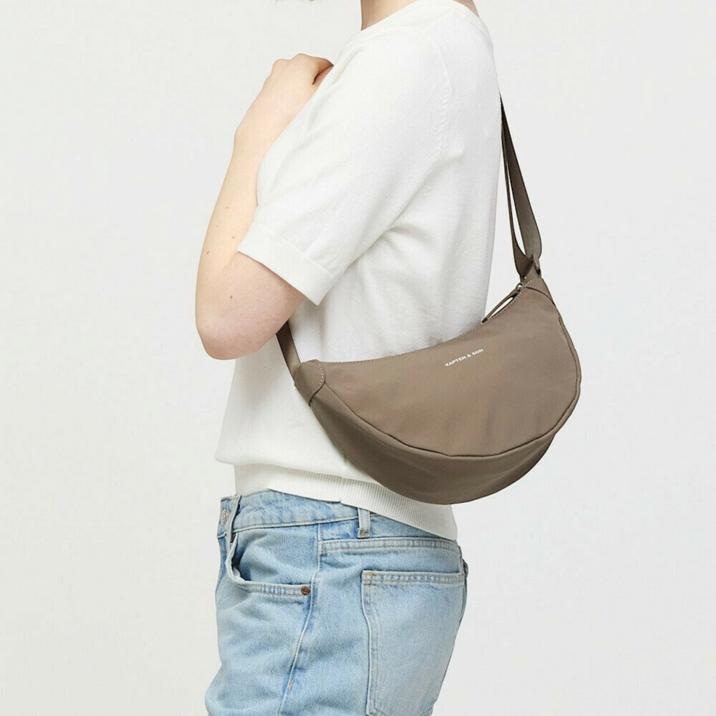 Lieblingstasche Essential Moon Bag in taupe worn over the shoulder by a woman in a white top and blue jeans