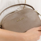 Lieblingstasche Style Mate taupe pebbled leather crossbody bag with gold hardware held by a person