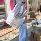 Lieblingstasche white and grey sailcloth tote bag with text detail, worn by a woman in a grey hoodie and jeans.